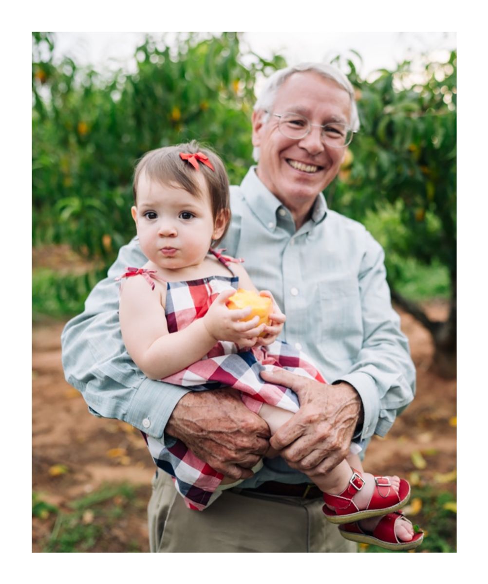 grandfather holding baby in peach orchard